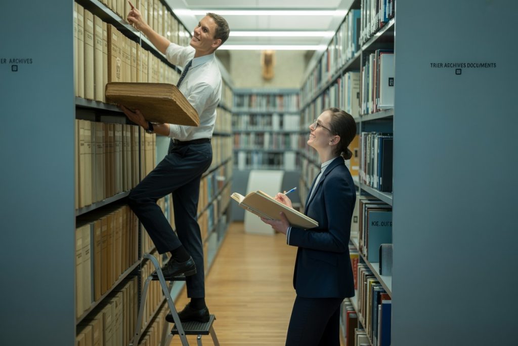 Archiviste tend un registre à une jeune femme dans les rayonnages d'archives municipales