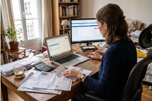 Personne faisant ses comptes et triant des courriers administratifs sur un ordinateur à la maison