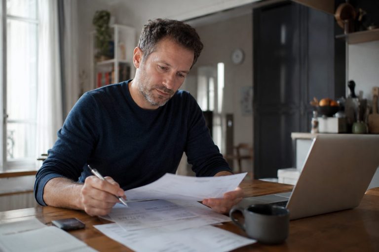 Une personne compare les taux de comptes à terme sur ses relevés bancaires et son ordinateur portable