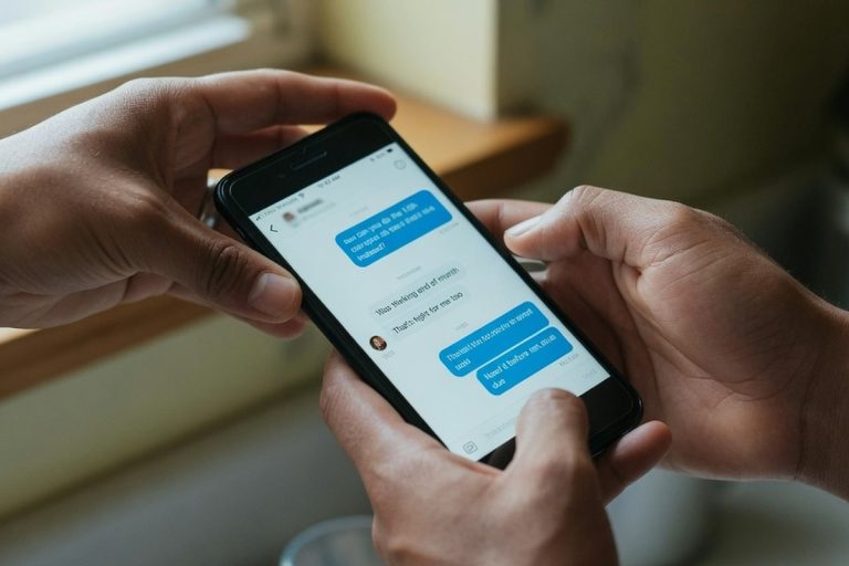 Mains tenant un smartphone affichant des messages dans une cuisine lumineuse